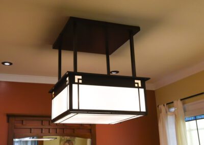 Modern lantern-style chandelier hanging in a room with warm-toned walls and ceiling recessed lights.