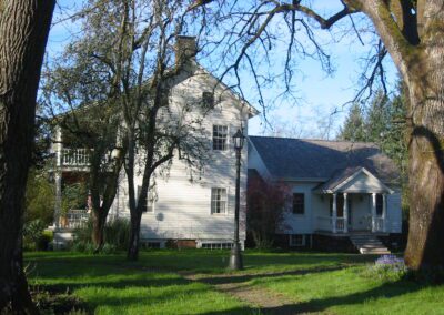 A traditional white house with a porch, surrounded by trees in a sunny garden setting.