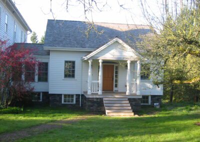 A traditional house with a front porch and a stone foundation surrounded by a green lawn and trees.