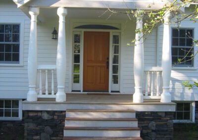 Front entrance of a white house with a wooden door and stone steps.