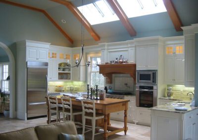 Spacious kitchen with white cabinetry, stainless steel appliances, and a center island under a skylight.